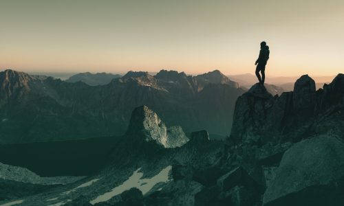 A silhouette of a person standing on the top of a hill under the beautiful colorful sky in the early morning